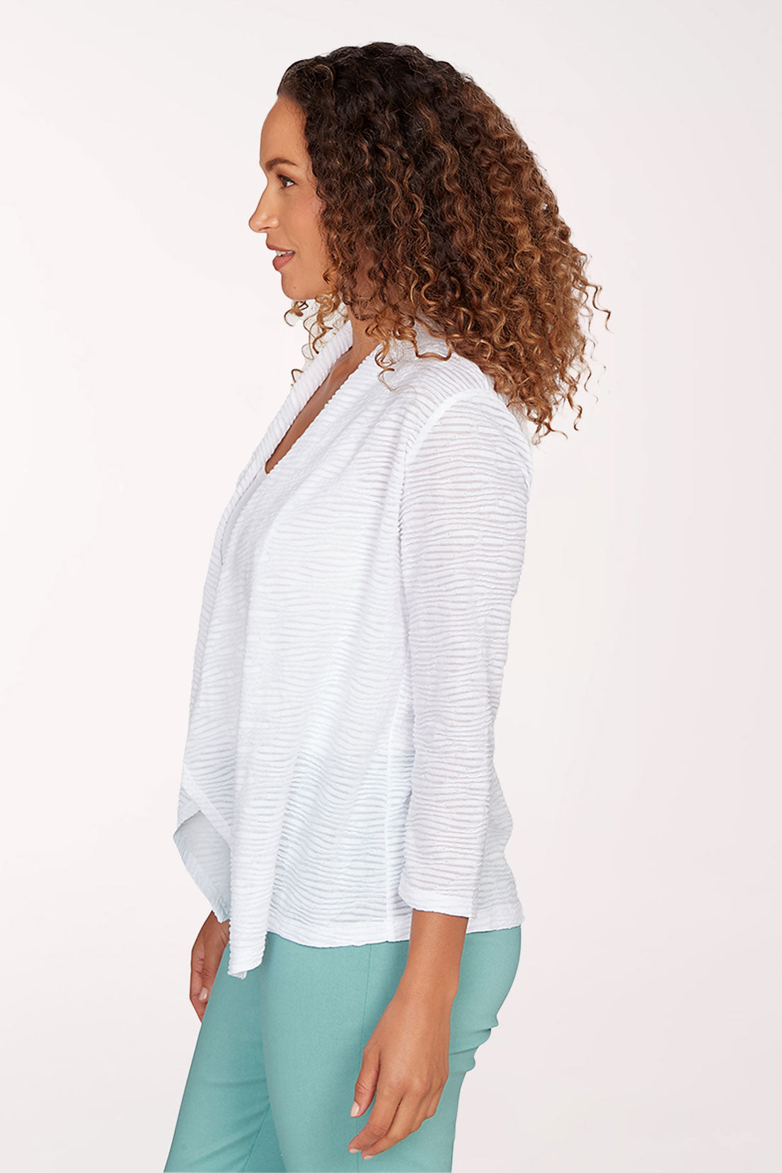 Woman wearing a white open-front cardigan over a white top and green pants on a light pink background