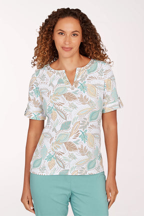 Woman wearing a patterned blouse and teal pants on a white background