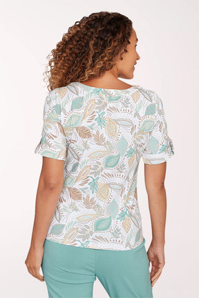 Woman wearing a patterned blouse and teal pants on a white background