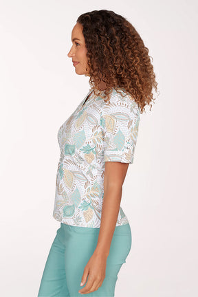 Woman wearing a patterned blouse and teal pants on a white background