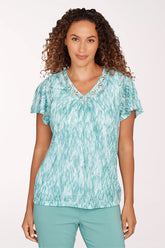 Woman wearing a teal patterned top and pants on a white background
