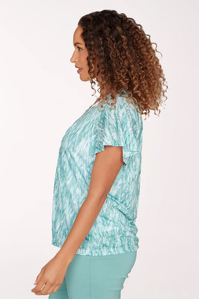 Woman wearing a teal patterned top and pants on a white background