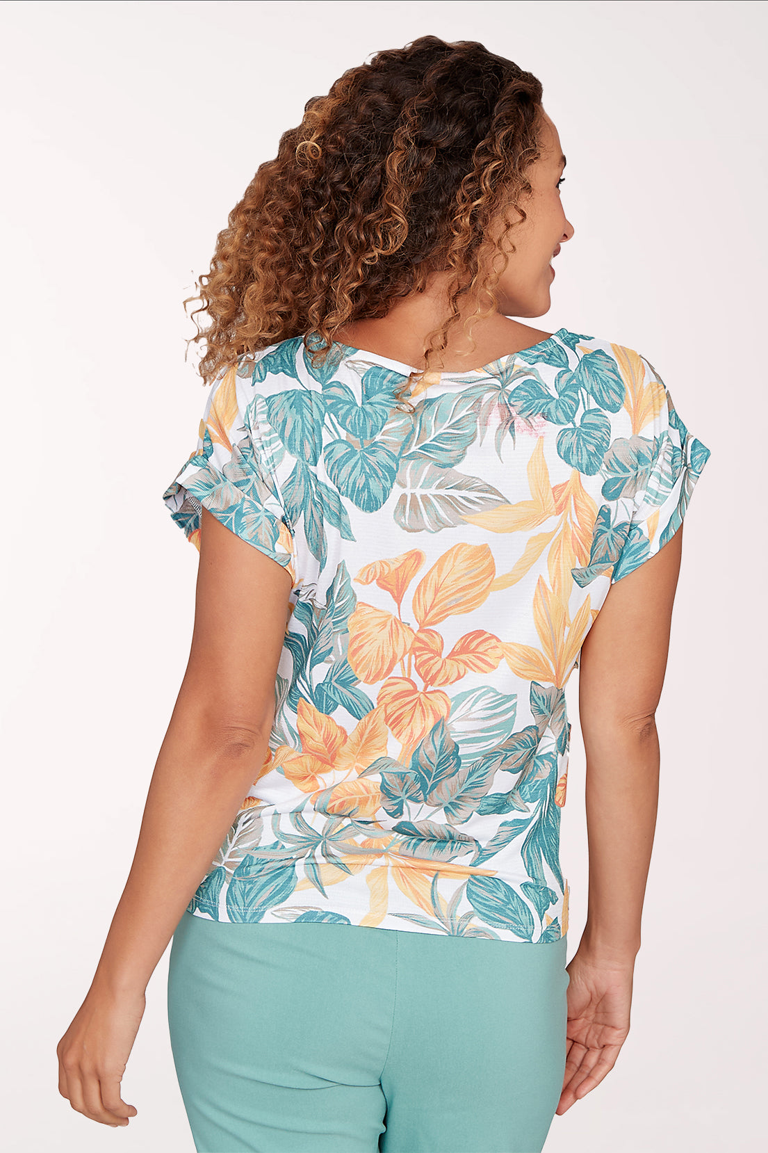 Woman wearing a short sleeve yellow and green leaf patterned top.