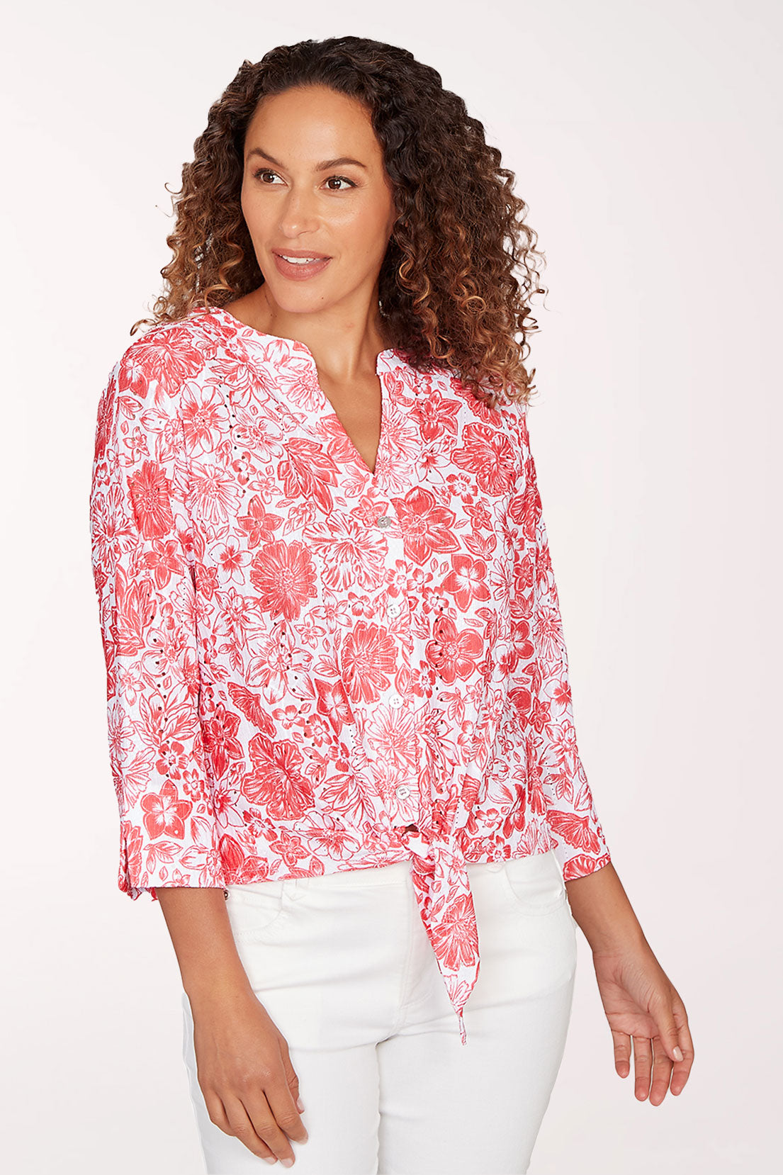 Woman wearing a red floral blouse and white pants on a white background