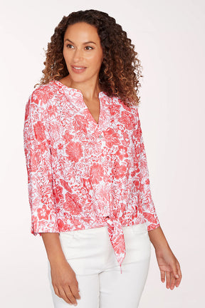 Woman wearing a red floral blouse and white pants on a white background
