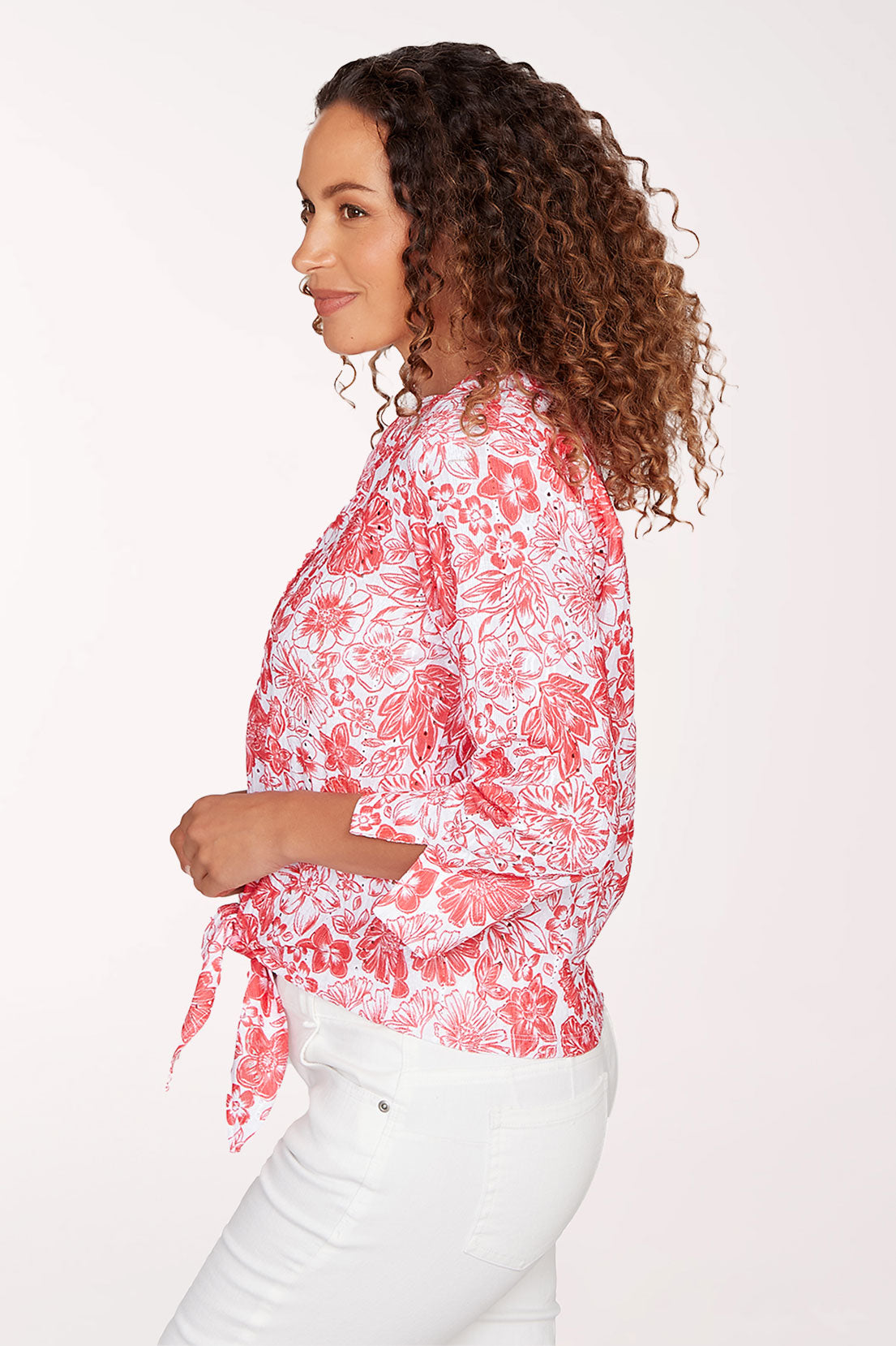 Woman wearing a red floral blouse and white pants on a white background
