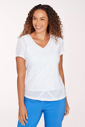 Woman wearing a white top with a subtle pattern and blue pants on a light pink background