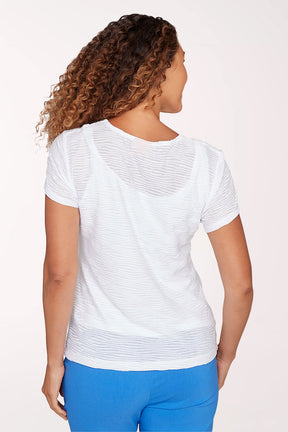 Woman wearing a white top with a subtle pattern and blue pants on a light pink background