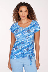 Woman wearing a blue patterned top and light blue pants on a white background