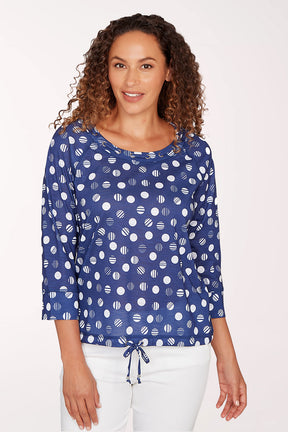 Woman wearing a blue patterned blouse with white pants on a light background