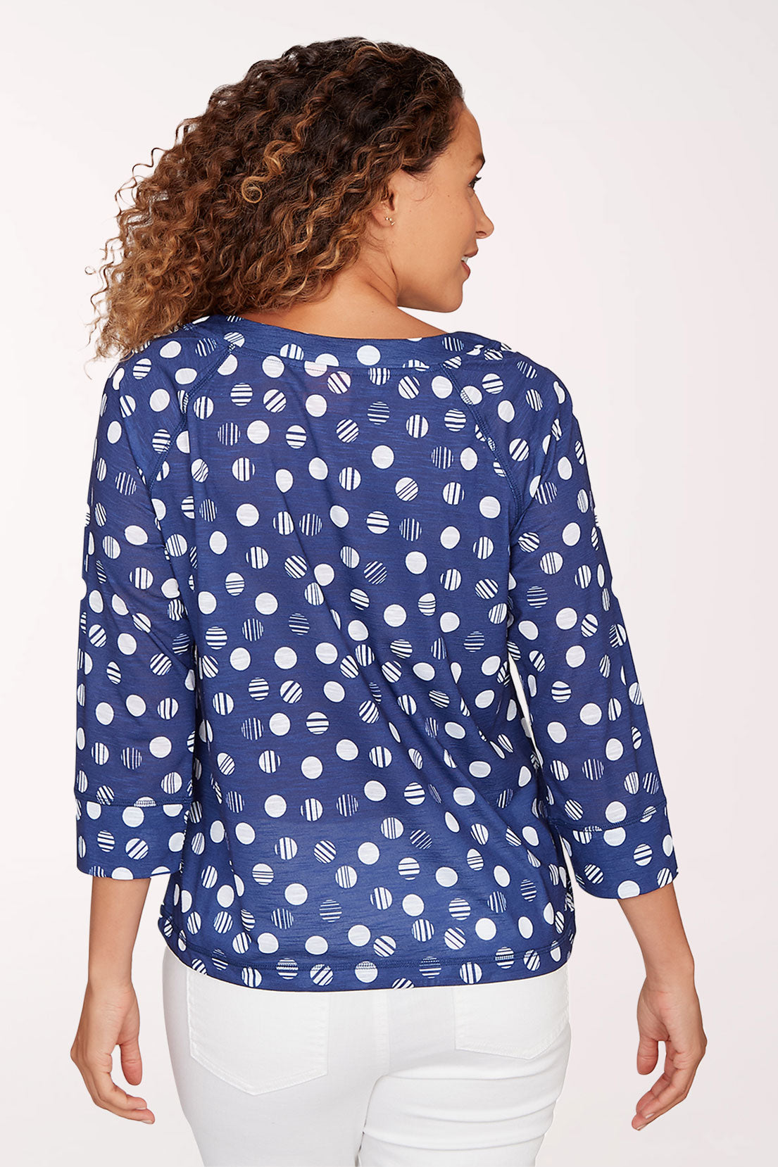 Woman wearing a blue patterned blouse with white pants on a light background