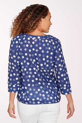 Woman wearing a blue patterned blouse with white pants on a light background