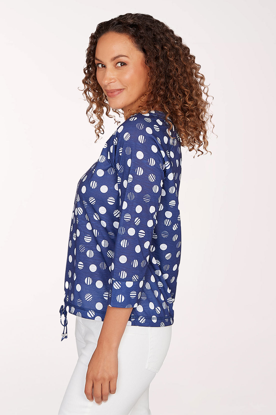 Woman wearing a blue patterned blouse with white pants on a light background