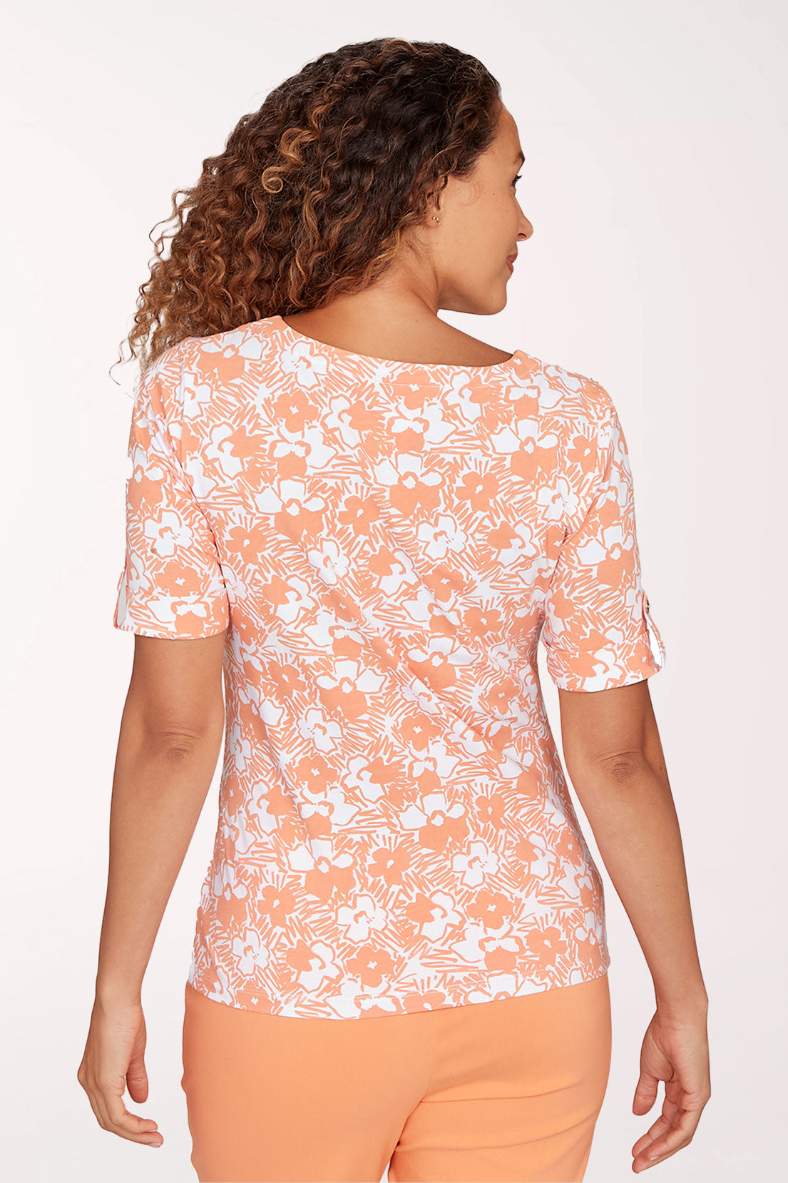 Woman wearing a floral patterned top and orange pants on a white background