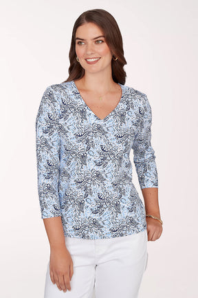 Woman wearing a blue patterned top with white pants on a plain background