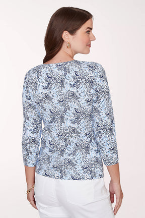 Woman wearing a blue patterned top with white pants on a plain background