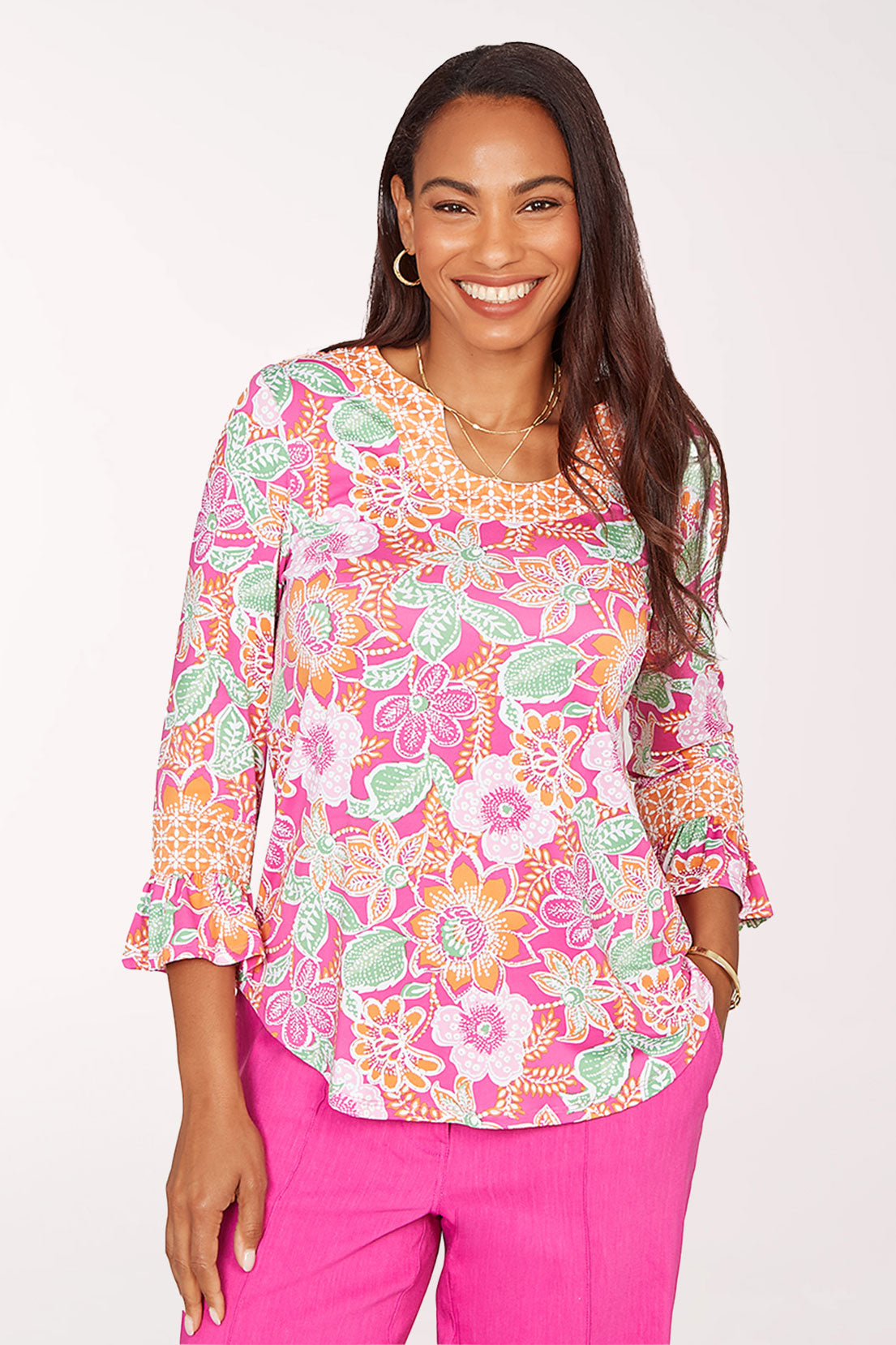 Woman wearing a colorful floral blouse and pink pants on a white background