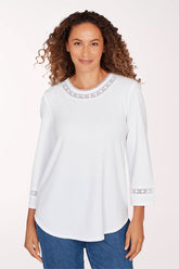 Woman wearing a white long-sleeve top with lace details on a light pink background