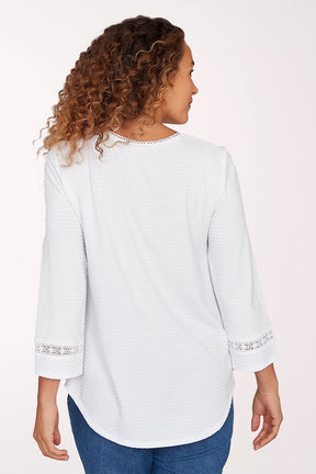 Woman wearing a white long-sleeve top with lace details on a light pink background