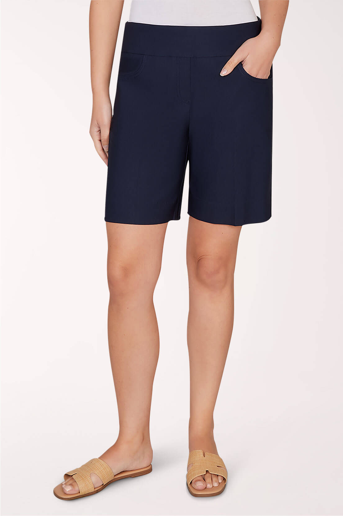 A person wearing navy blue shorts and sandals against a light pink background