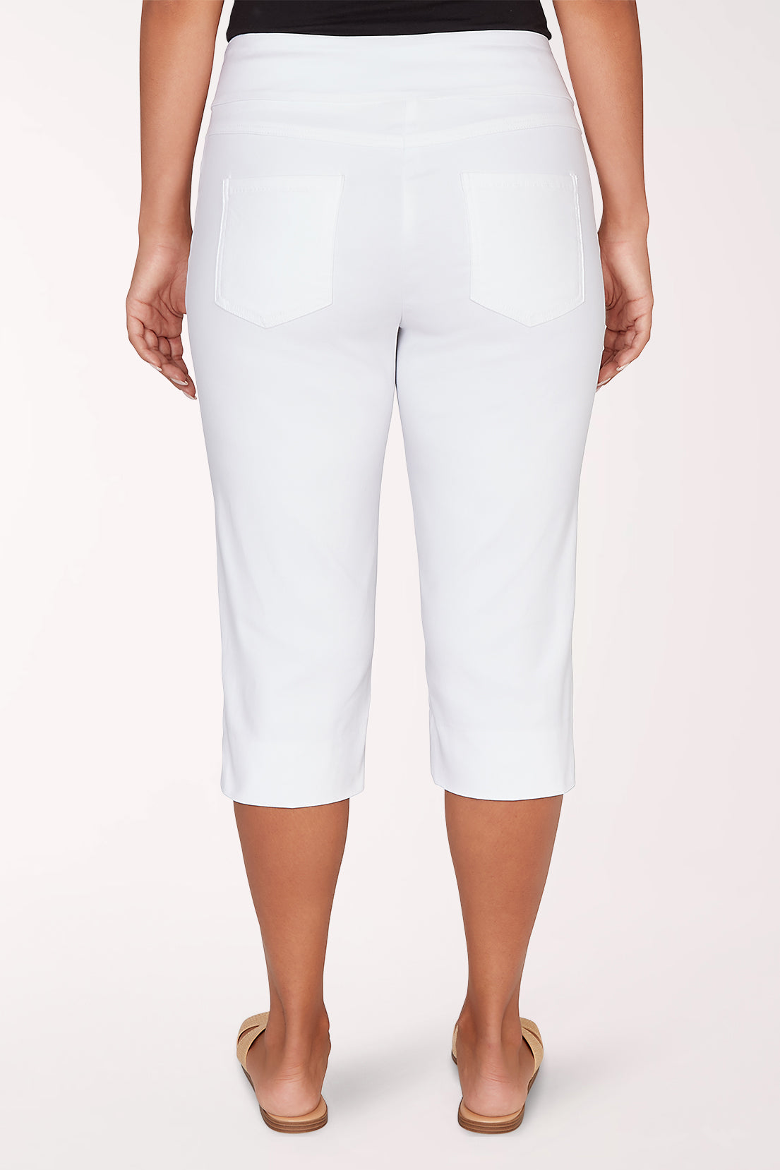 Person wearing white capri pants on a light pink background