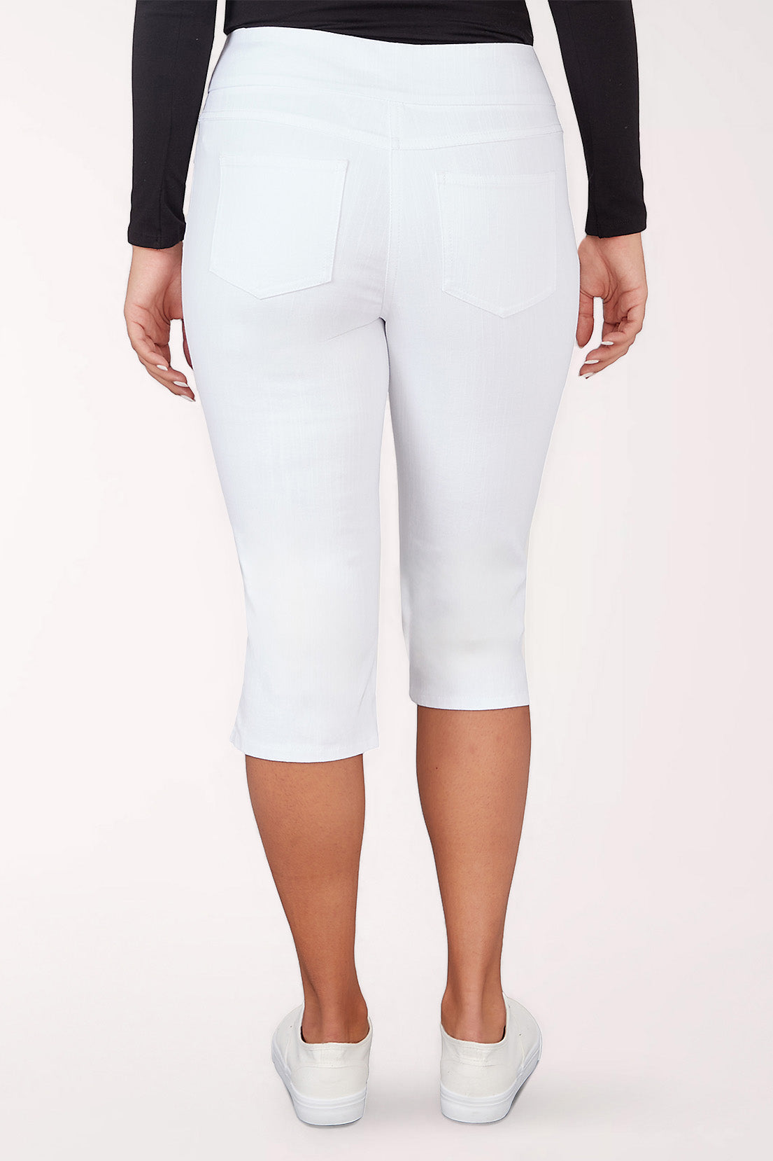 Person wearing white capri pants on a light pink background