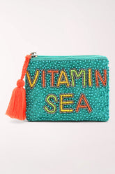A turquoise beaded zip pouch with 'VITAMIN SEA' spelled out in colorful rhinestone letters and a bright orange tassel zipper pull, shown on a light gray background.