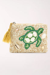A square zippered clutch bag covered in beige seed beads, featuring a green turtle design with white shell details, small seashell embellishments, and a yellow tassel on the zipper.