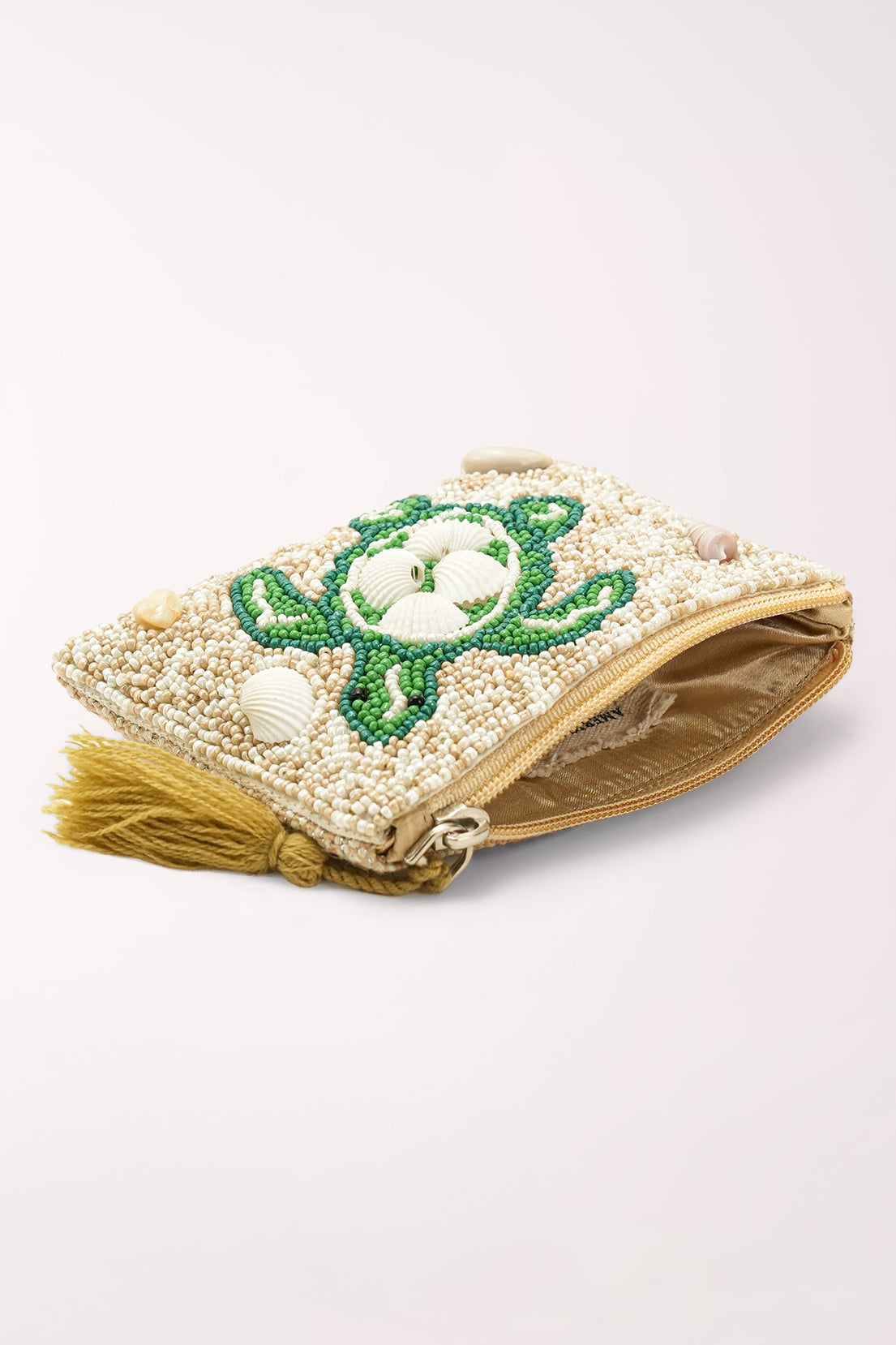 A small zippered clutch bag with a cream-colored beaded surface, featuring a green turtle design made from green and white beads, a white seashell accent, and a gold tassel on the left side.