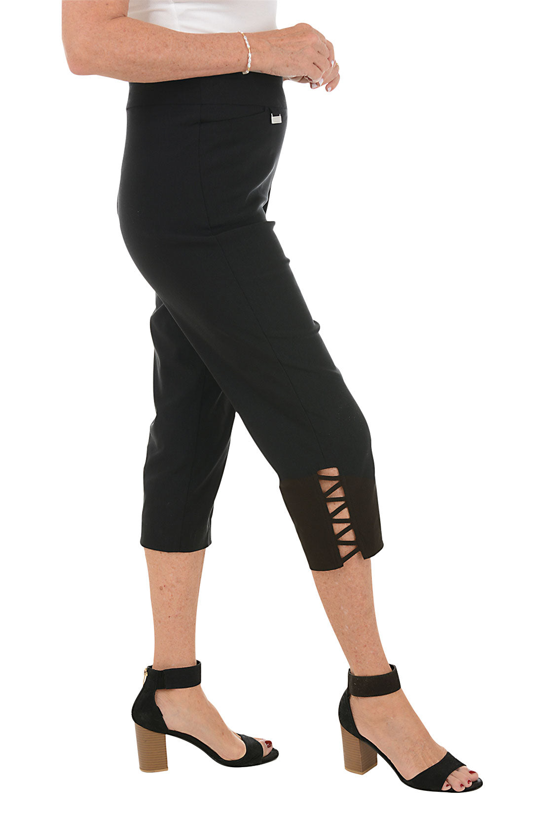 Person wearing black capri pants with lattice detail on side hem on a white background. Side shot.