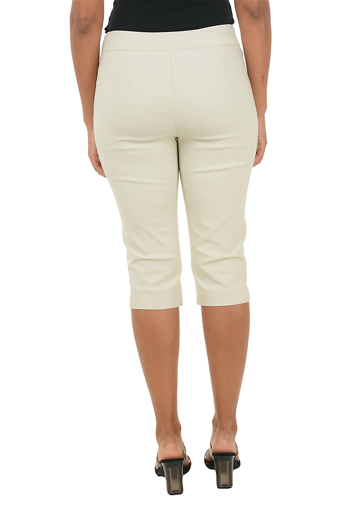 A person shown from the back wearing cream-colored capri pants with a black top and black heeled sandals, against a plain white background.
