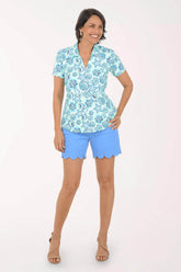 Woman wearing a blue patterned shirt and light blue shorts on a white background
