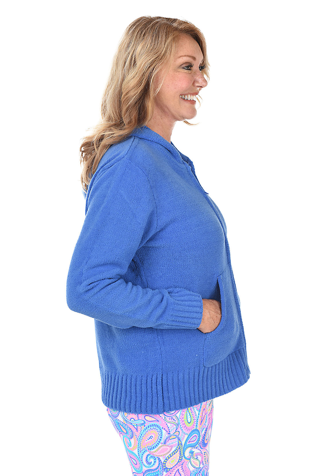 Woman wearing a blue zip-up hoodie and colorful patterned leggings on a white background. Side shot.