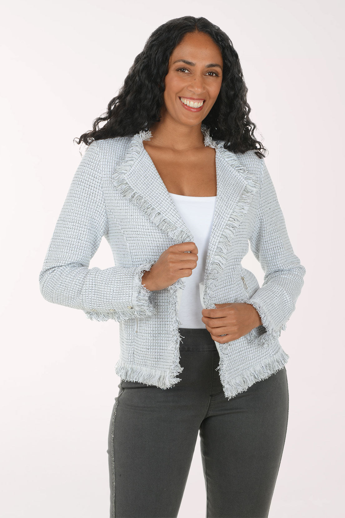 A woman modeling a light blue and white textured tweed jacket with frayed edges, worn over a white top and dark gray pants, against a plain white studio background.