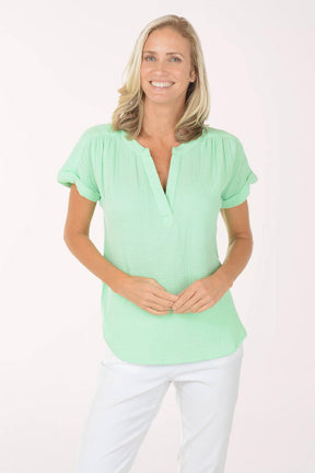 Woman wearing a light green blouse and white pants on a plain background