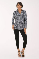 A woman modeling a long-sleeve button-up blouse with a black, white, and gray paisley pattern, paired with black cropped pants and black strappy high-heeled sandals, against a plain white studio background.
