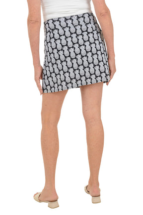 Person wearing a black and white pineapple patterned skirt on a white background. Back shot.