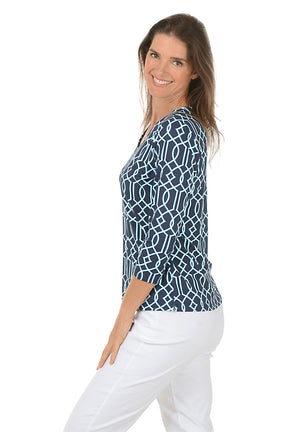 Woman wearing a blue patterned top and white pants on a white background. Side shot.