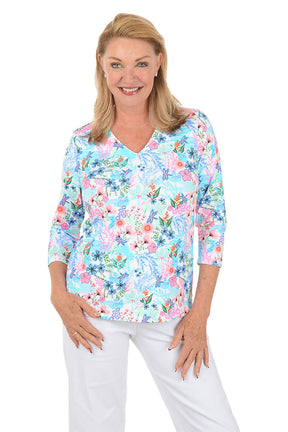 Woman wearing a floral blouse with white pants on a white background. Second front shot.