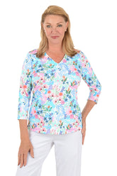 Woman wearing a floral blouse with white pants on a white background.