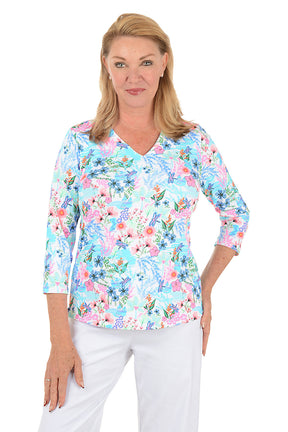 Woman wearing a floral blouse with white pants on a white background.
