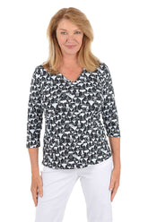 A woman wearing a black and white cocktail patterned v-neck 3/4 sleeve top with silver foil accents.