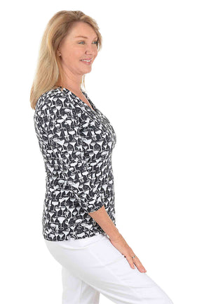 A woman wearing a black and white cocktail patterned v-neck 3/4 sleeve top with silver foil accents. Side shot.