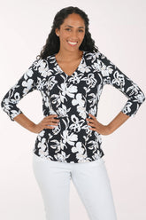A woman modeling a black and white floral print top with three-quarter sleeves and white pants, standing against a plain light background.