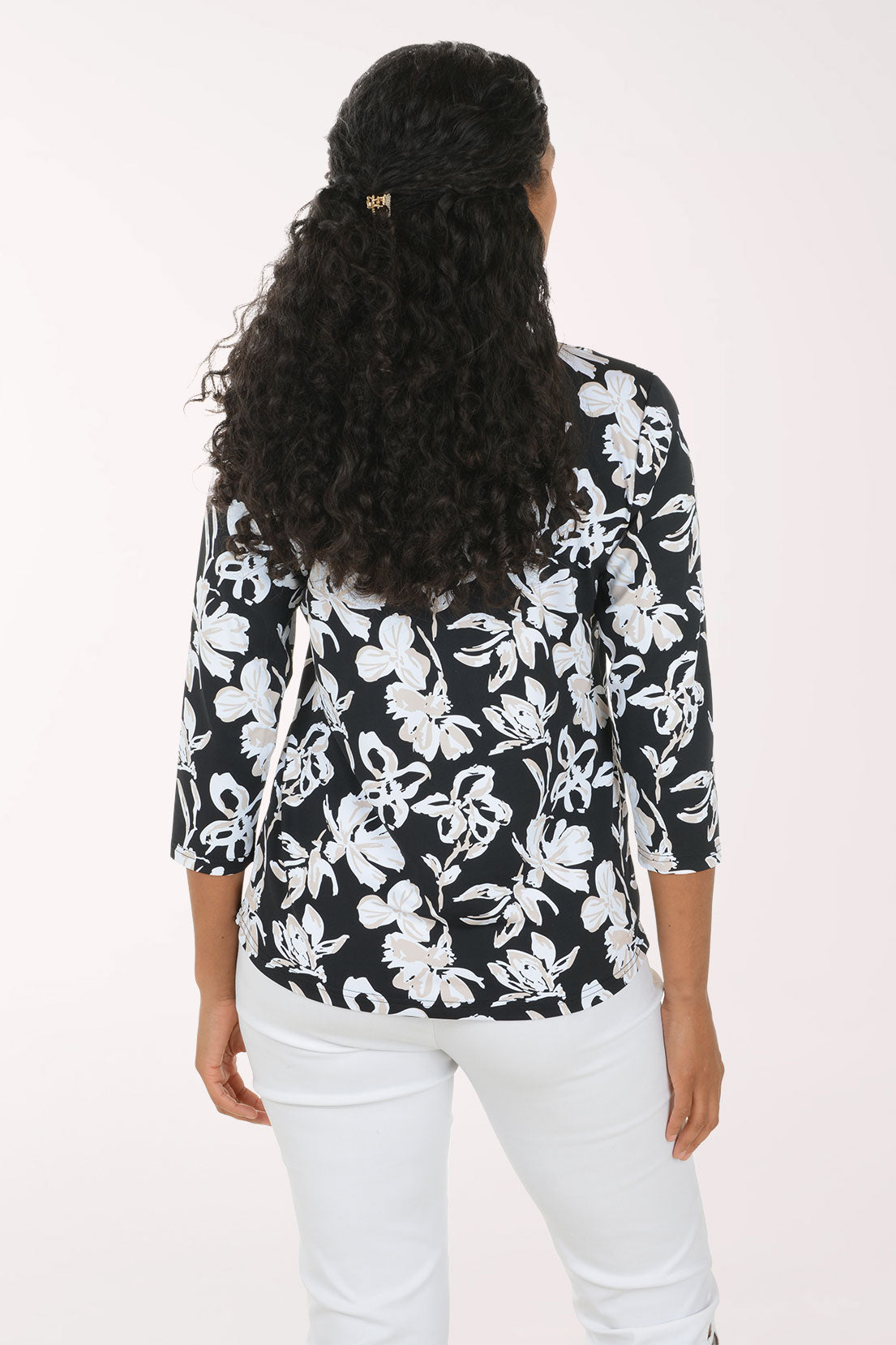 A woman modeling a black and white floral print top with three-quarter sleeves and white pants, standing against a plain light background.