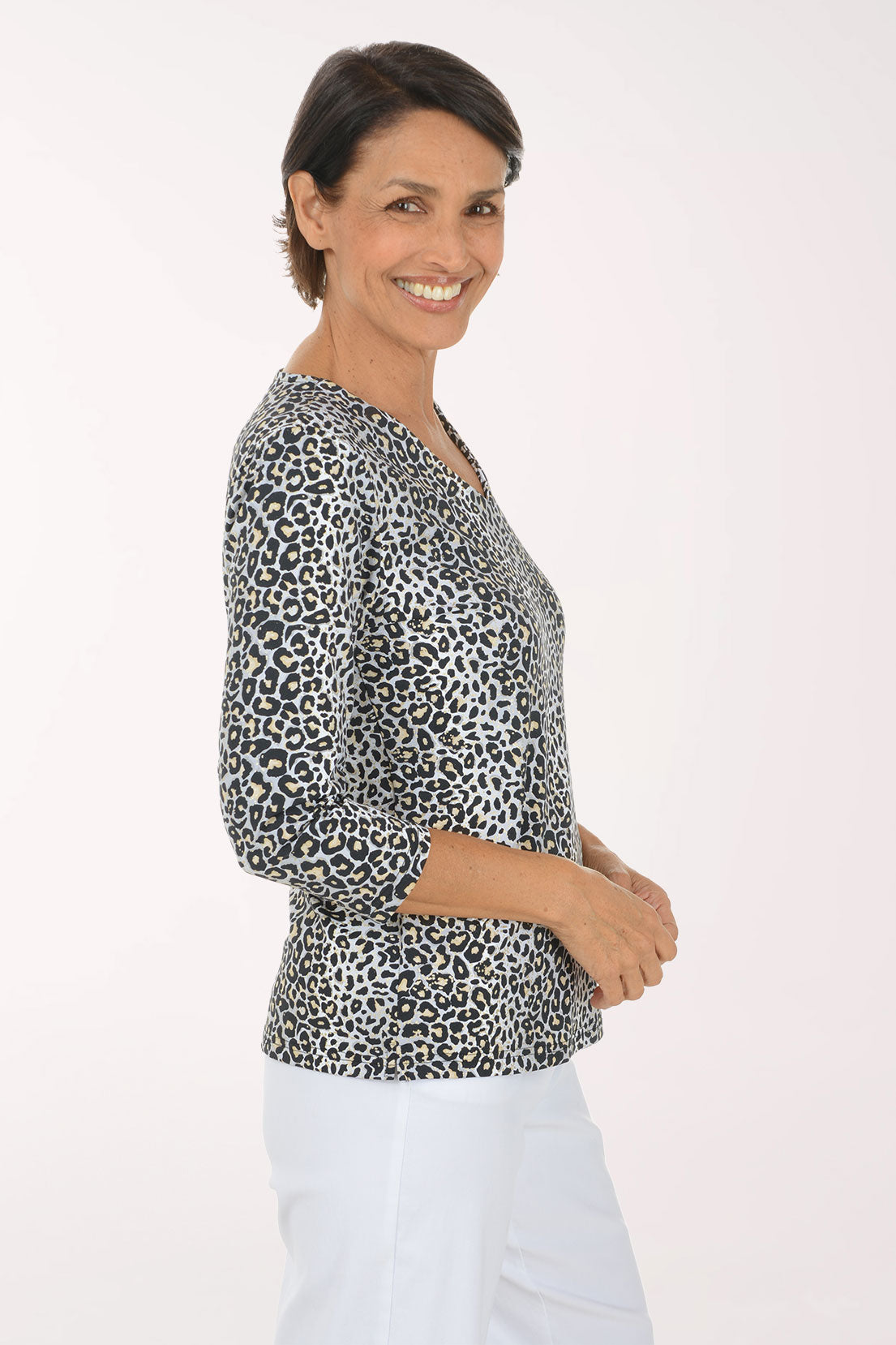 A woman modeling a black and white leopard print long-sleeve top with a V-neck, paired with white pants, against a plain light background.