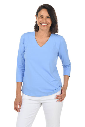 Woman wearing a light blue long-sleeve top and white pants on a white background