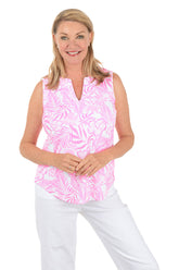 Woman wearing a pink sleeveless top with a leaf pattern and white pants on a white background.