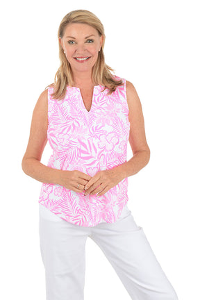 Woman wearing a pink sleeveless top with a leaf pattern and white pants on a white background.