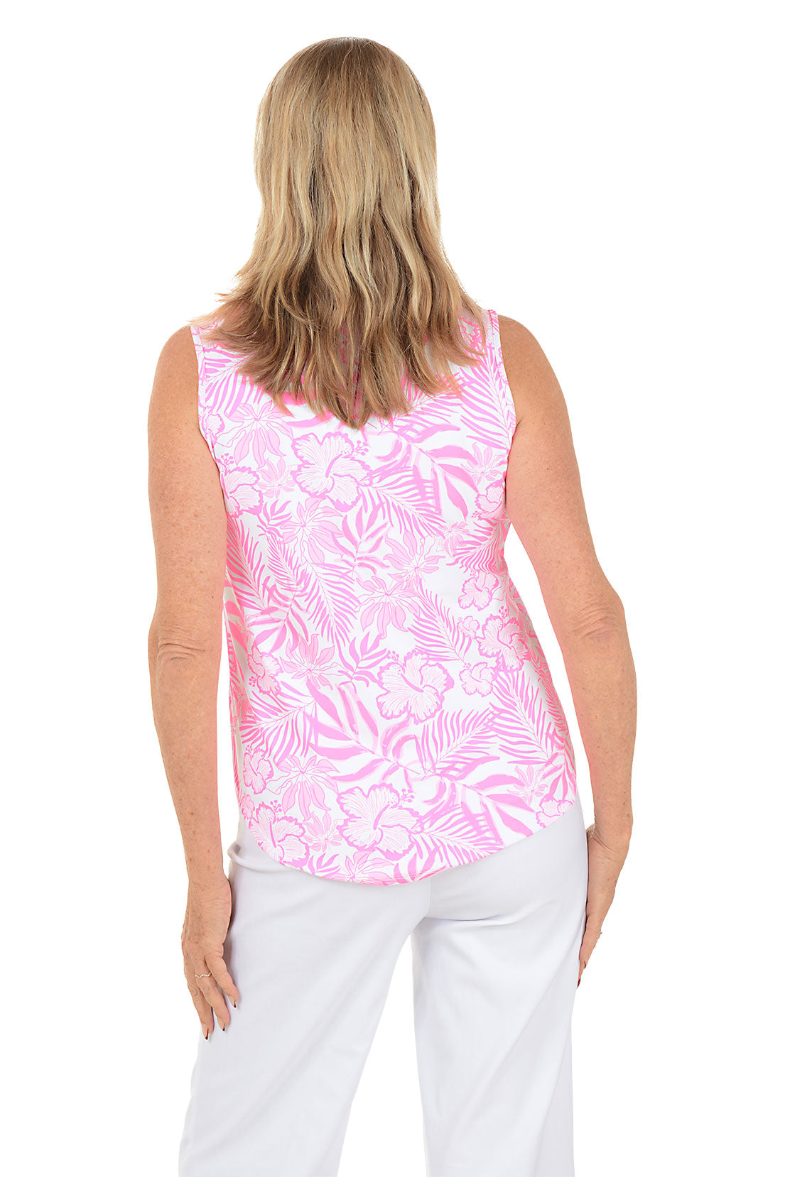 Woman wearing a pink sleeveless top with a leaf pattern and white pants on a white background. Back shot.